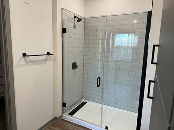 A white tiled shower in a bathroom with a glass door
